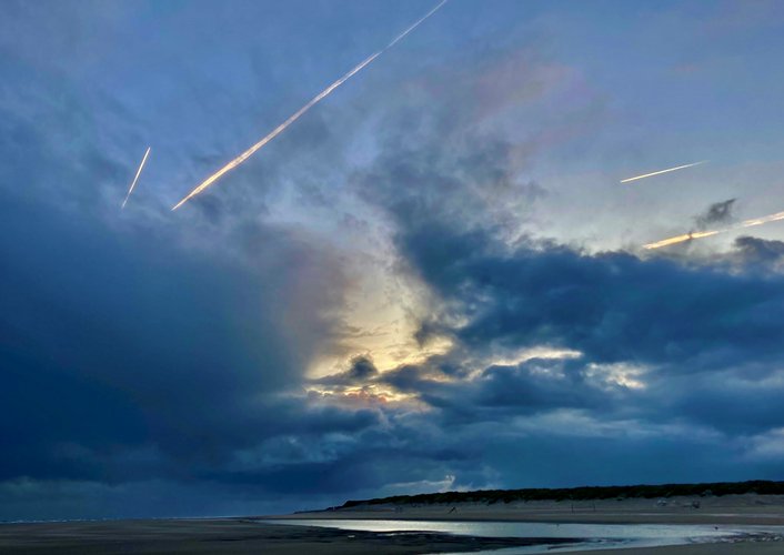 Dunkle Wolken mit einem hellen Sonnenstrahl über einem Strand